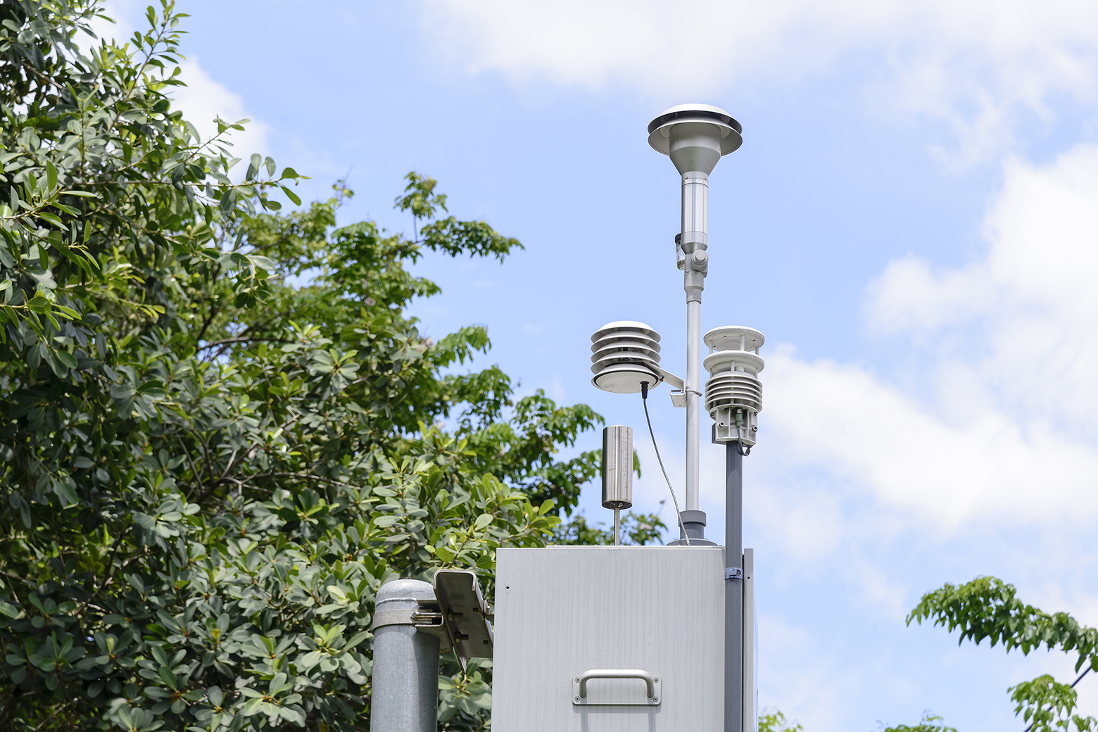 A compact air-quality sensor station mounted on a roadside pole above traffic.